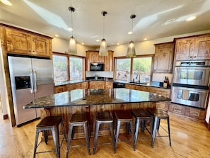 A kitchen with wooden cabinets, stainless steel appliances, a large island with stools, and pendant lighting.