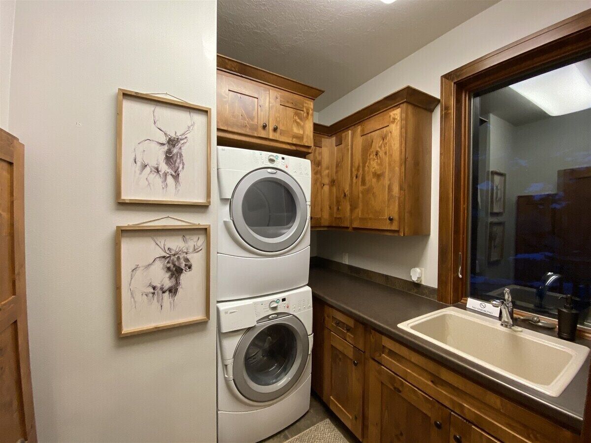 A laundry area with stacked washers and dryers, wooden cabinets, a sink, and framed artwork on the wall.