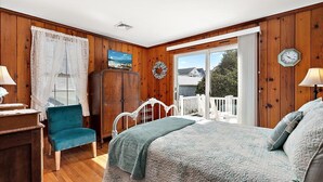 Une chambre à coucher comprenant un lit, une chaise, une armoire, une fenêtre avec des rideaux, une porte et une vue sur l’extérieur.