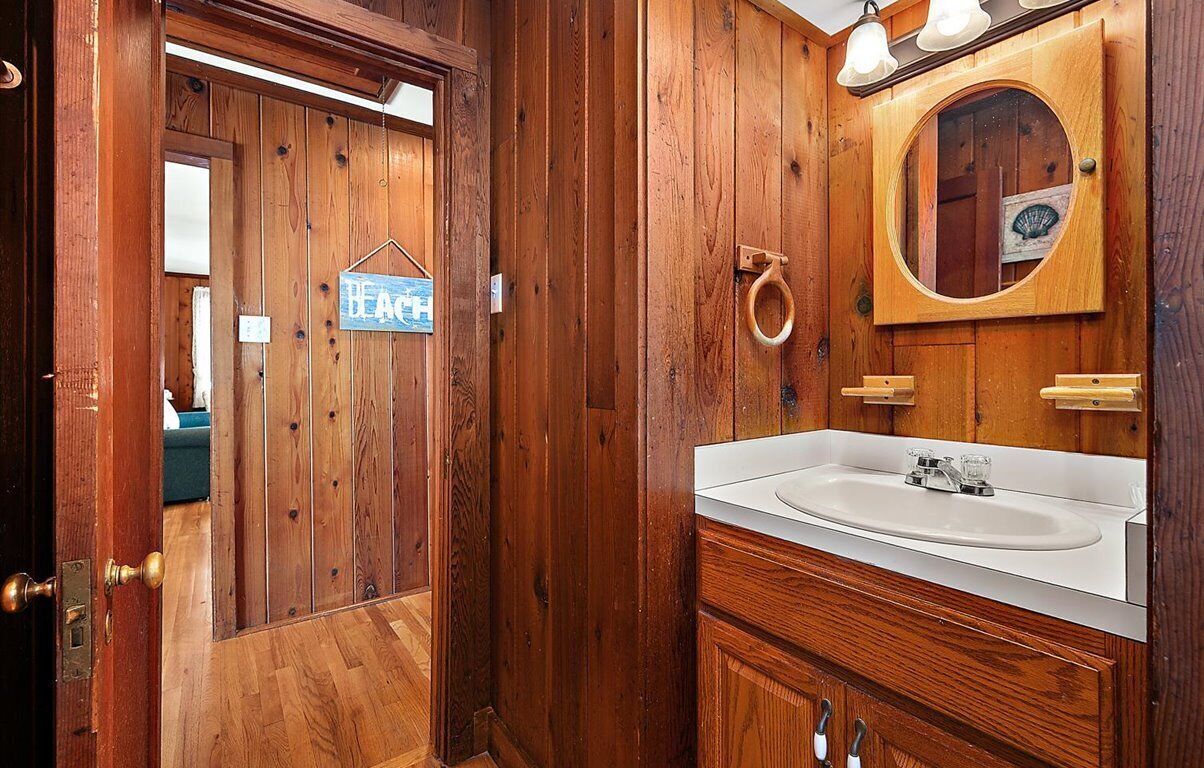 Un baño de madera con un lavabo blanco, un espejo redondo y una puerta con un cartel que dice 'BEACH'.