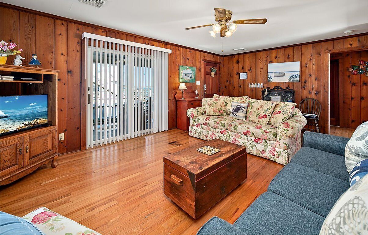 Un salon avec des murs en bois, un canapé, une table basse, un téléviseur et un ventilateur de plafond.