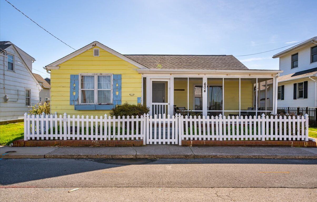 A yellow house with a white picket fence, a porch, and a number '604' on the door.
