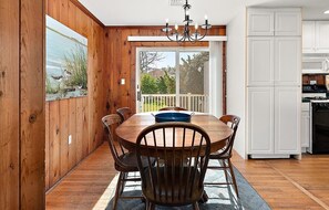 A wooden dining room with a large table and chairs, a chandelier, and a view of the outdoors through a sliding glass door.