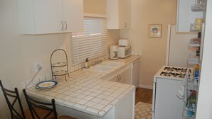 A compact kitchen with a sink, stove, and microwave. There are chairs and a small dining table. - Beach Cottage - 4th from Ocean, Private Patio, Ocean View, now with A/C (San Diego)