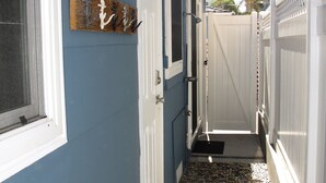 A narrow outdoor corridor with a blue wall, white doors, and a wooden art piece. - Beach Cottage - 4th from Ocean, Private Patio, Ocean View, now with A/C (San Diego)