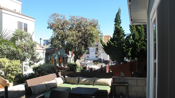 A courtyard with a green sofa, a wicker table, and a potted plant. There is a tree in the background and a building with a sign. - Beach Cottage - 4th from Ocean, Private Patio, Ocean View, now with A/C (San Diego)