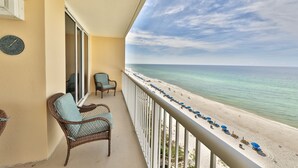 A balcony with wicker chairs and a view of a beach with umbrellas.
