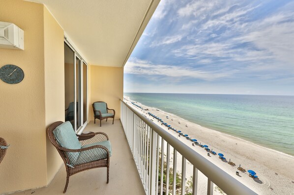 A balcony with wicker chairs and a view of a beach with umbrellas.