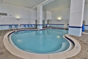 Ein beheizter Innenpool mit klarem, blauem Wasser, einer gefliesten Liegefläche und einigen Liegestühlen.