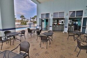 Ein Außenbereich mit Terrassentischen und -stühlen, einem Pool und einer Bar.
