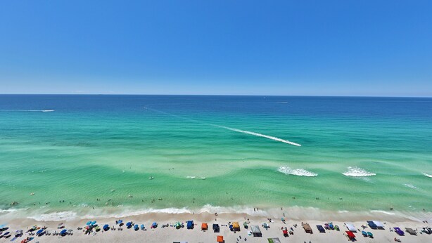 A beach with clear turquoise waters, a sandy shore, and numerous umbrellas and beach chairs.