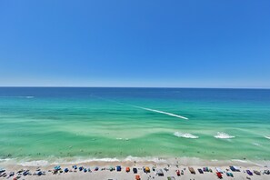 A beach with clear turquoise waters, a sandy shore, and numerous umbrellas and beach chairs.