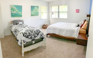 Une chambre avec deux lits, une fenêtre et des œuvres d’art accrochées au mur.