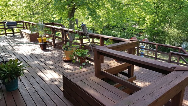 Eine Holzterrasse mit Geländern, Blumentöpfen und einem Grill.