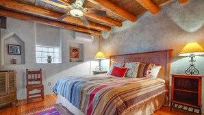 Un dormitorio con techo de madera, una cama con manta a rayas de colores, dos lámparas de noche y una mesita de noche de madera.