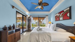 Un dormitorio con una cama, un armario de madera, un ventilador de techo, un cuadro y vistas al océano.