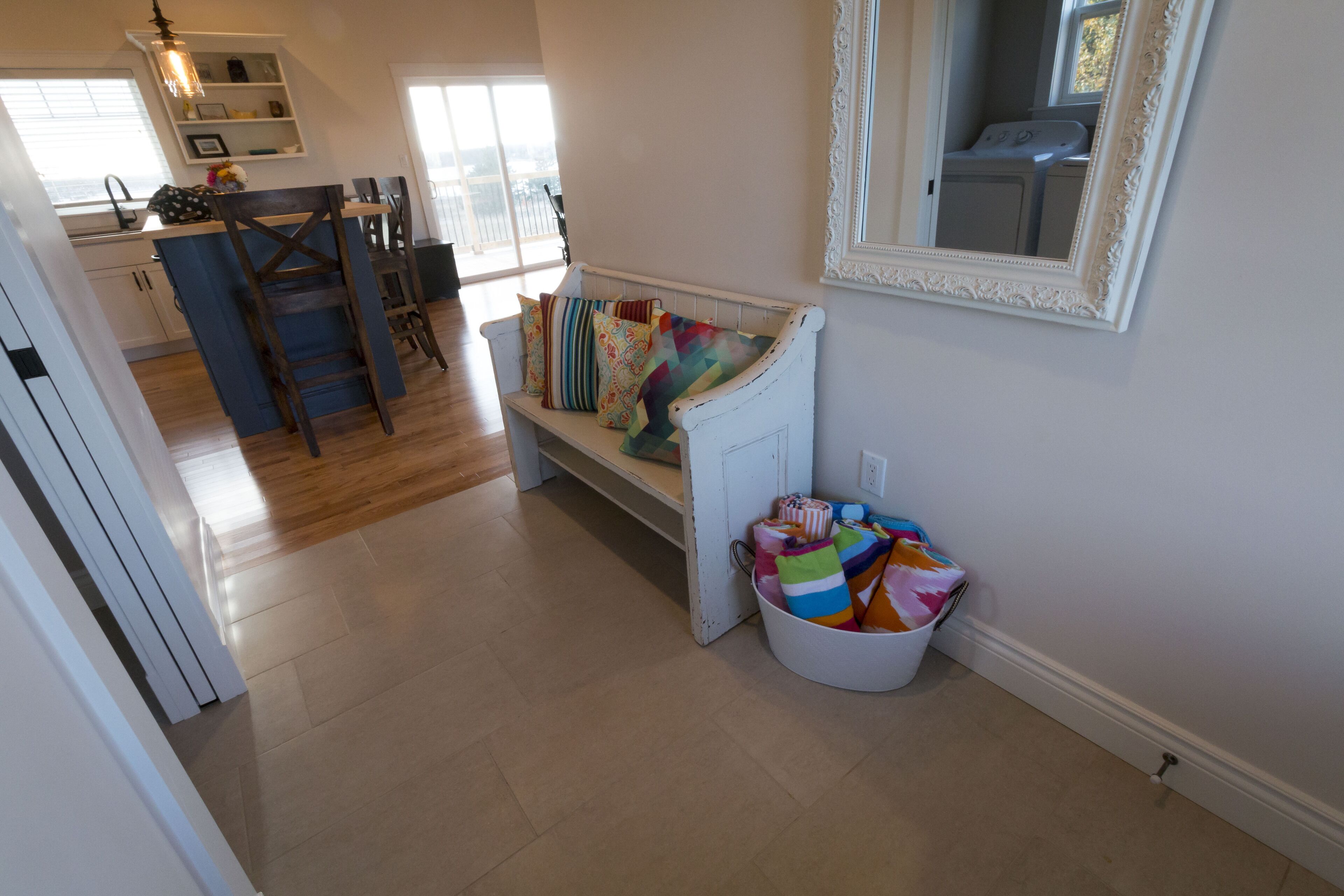A spacious living area with a wooden bench, a white wall-mounted mirror, and a laundry basket filled with colorful items.