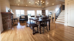 Un vaste salon doté d’un plancher en bois, d’une cheminée en pierre, d’une table à manger avec des chaises et d’un escalier menant à un autre niveau.