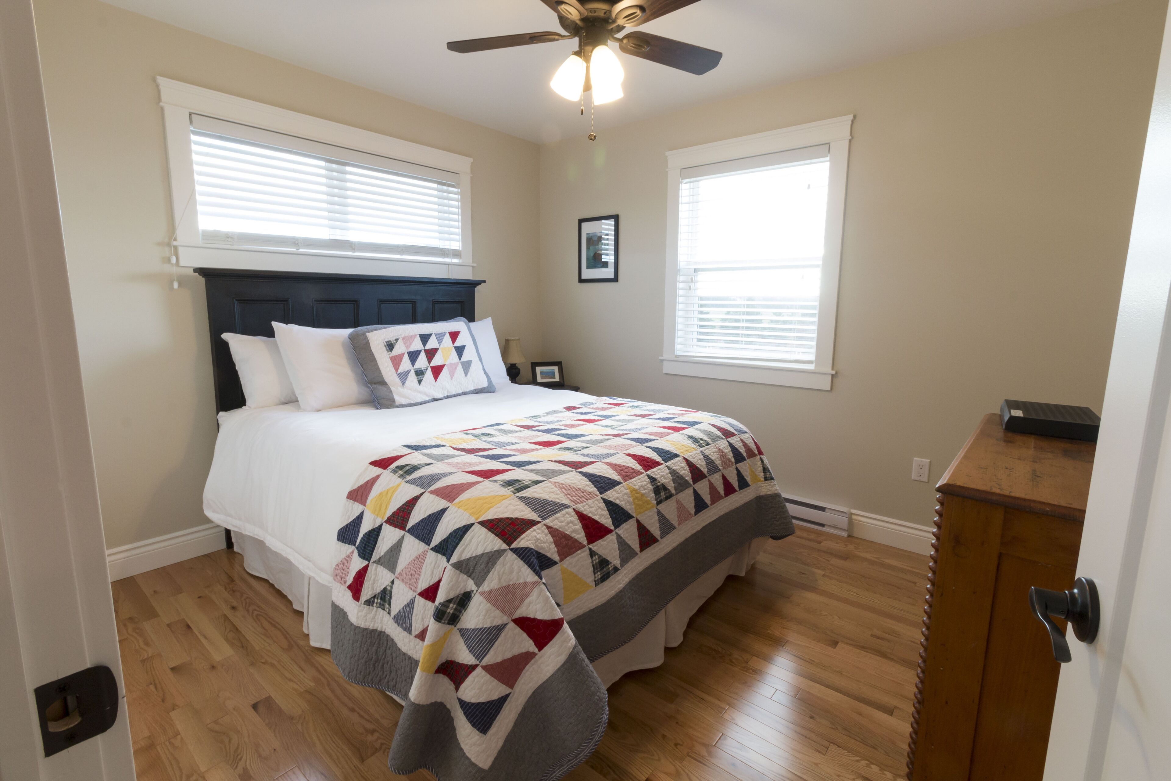 A bedroom with a bed, a ceiling fan, and a wooden dresser.
