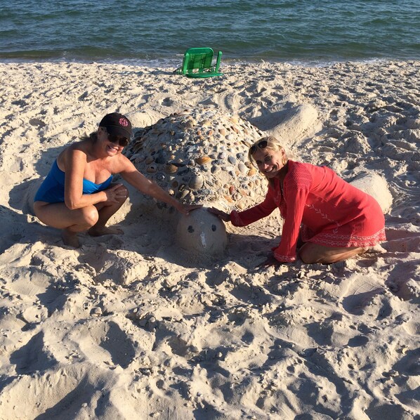Two people building a sandcastle on a beach with a green chair in the background.
