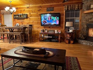 Cozy living room with a stone fireplace, flat-screen TV, and dining area.
