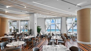 A modern dining area with tables set for guests, large windows with ocean views, and a wooden floor pattern. - Ocean view Penthouse in Palm Beach Singer Island Resort & Spa Luxury 2/2 unit 1912 (Singer Island)
