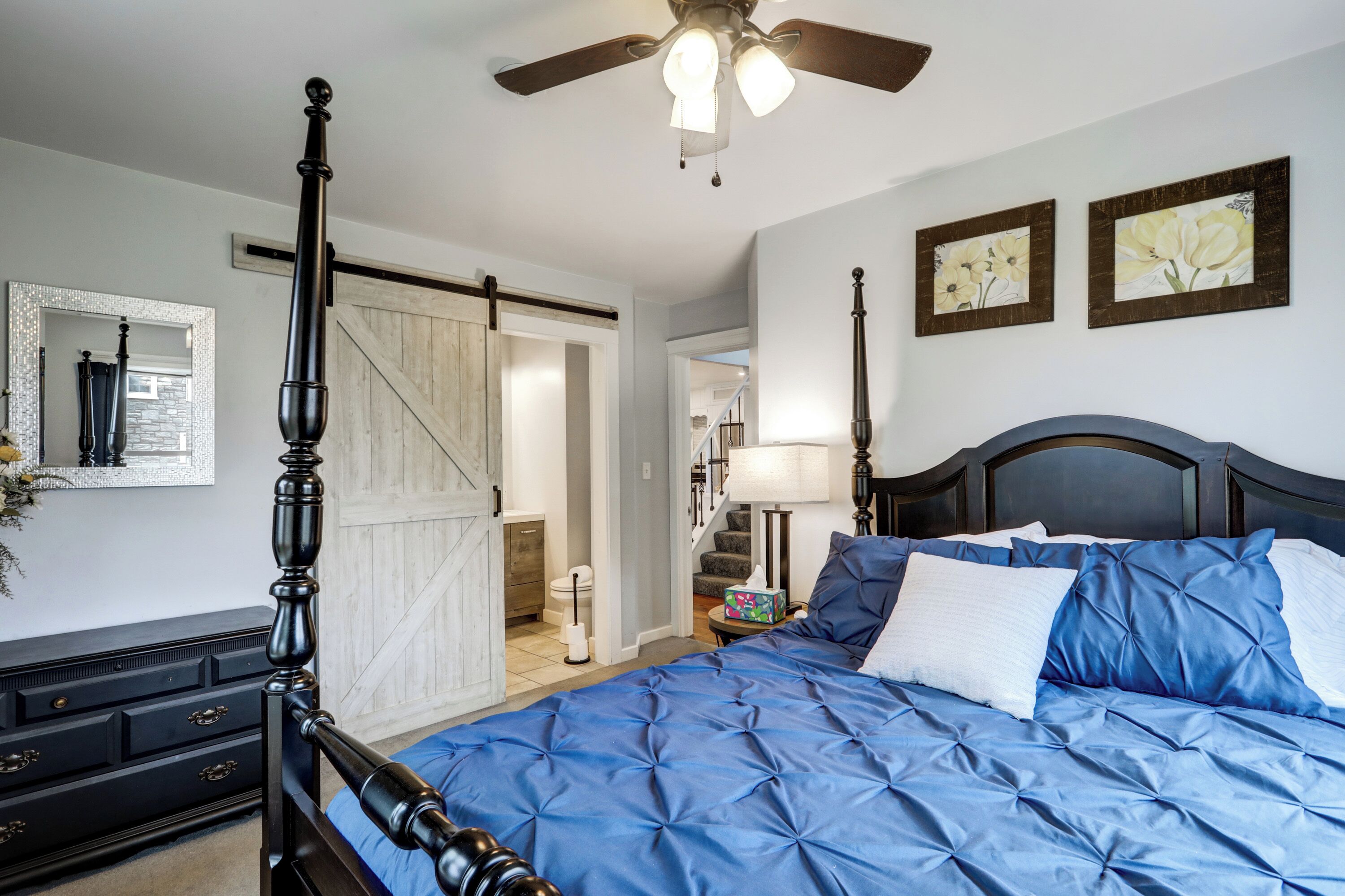 Une chambre à coucher avec un lit à baldaquin, un ventilateur de plafond, une commode et un miroir.