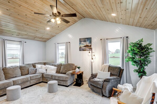 A spacious living room with a wooden ceiling, large windows, and a view of the outdoors.