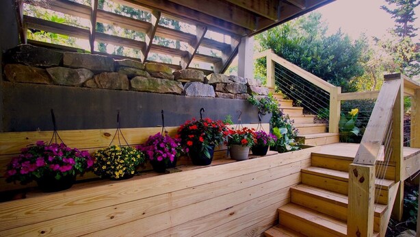 Un escalier en bois mène à un mur de pierre orné de jardinières suspendues.
