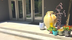 L’entrée d’un bâtiment est agrémentée de grandes portes vitrées, d’un grand vase en céramique, d’une sculpture en métal et de plusieurs plantes en pot.