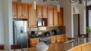 A kitchen with wooden cabinets, stainless steel appliances, a granite countertop, and pendant lights. - Tropical Villa with Spectacular Views!   (Dominical)