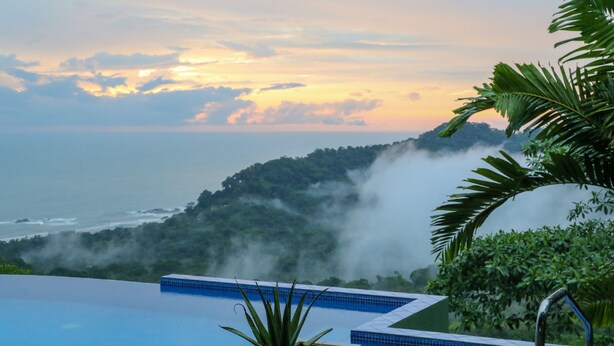 A pool with a view of the ocean and a misty hill in the background. - Tropical Villa with Spectacular Views!   (Dominical)