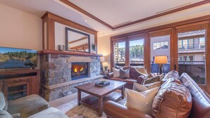 A cozy living room with a stone fireplace, leather sofa, and a television mounted on the wall. - Cozy Village at Northstar Condo w/ Peek-A-Boo View of Skating Rink! (Truckee)