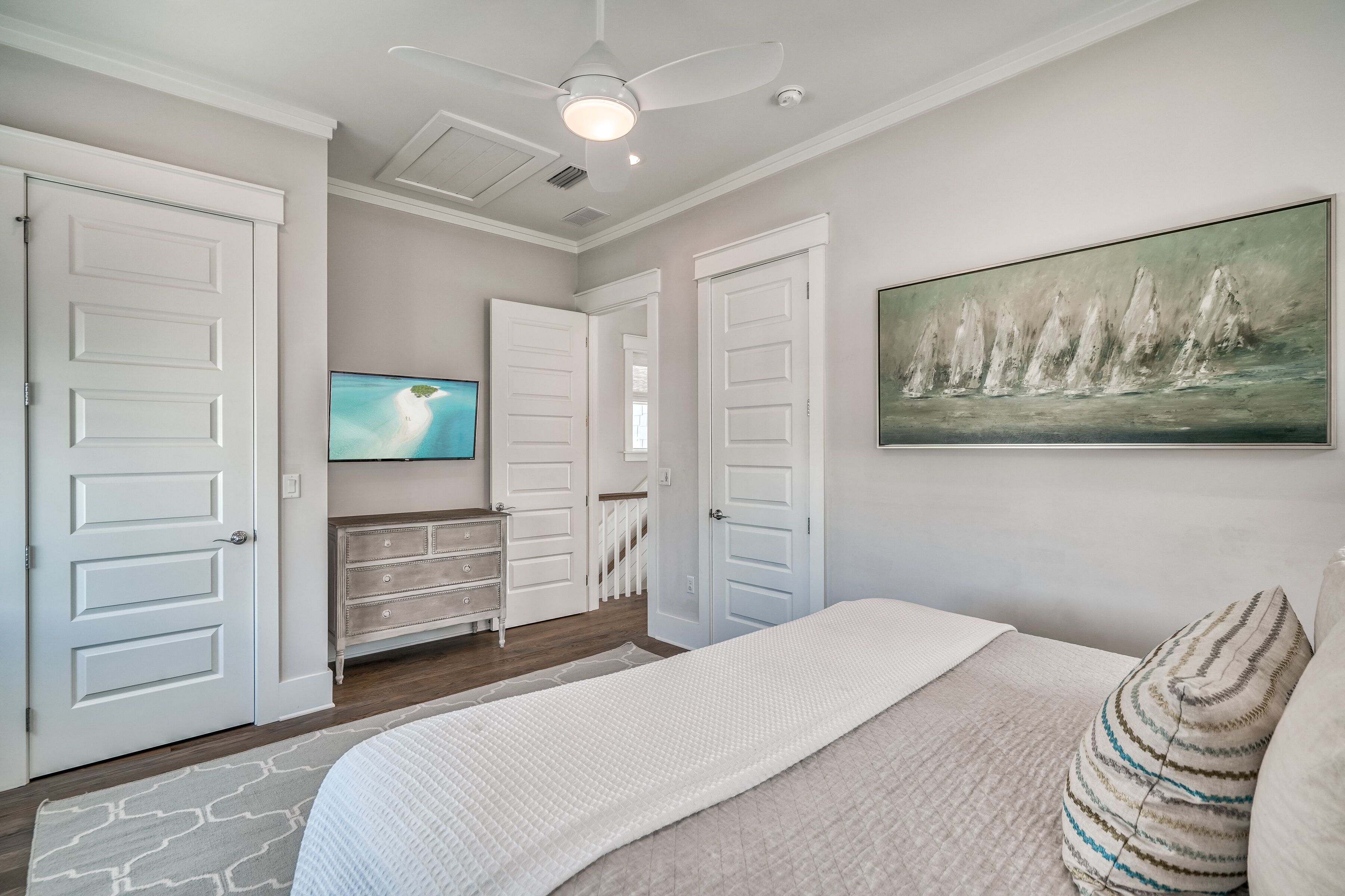 A bedroom with a bed, a television, a painting, and a staircase.