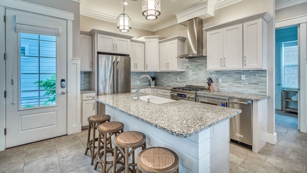 A modern kitchen with granite countertops, stainless steel appliances, and a large island with bar stools. - Lavish Coastal Getaway w/Media Room | 3 Min to Beach | Steps to Pool | 6 Bikes (Inlet Beach)