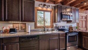 A modern kitchen with dark wood cabinets, stainless steel appliances, a granite countertop, and a window providing natural light. - Suzie's Luxury Cabin Asheville HOT TUB  VIEWS  nr BILTMORE. (Asheville)