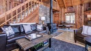 A rustic cabin interior with a stone fireplace, wooden staircase, leather sofas, and a dining area. - Suzie's Luxury Cabin Asheville HOT TUB  VIEWS  nr BILTMORE. (Asheville)