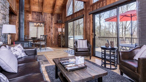 A spacious living room with a fireplace, large windows, and a deck area with outdoor furniture. - Suzie's Luxury Cabin Asheville HOT TUB  VIEWS  nr BILTMORE. (Asheville)