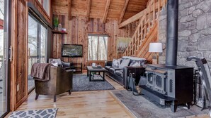 A cozy cabin interior with a stone wall, wooden ceiling, a fireplace, leather furniture, and a television. - Suzie's Luxury Cabin Asheville HOT TUB  VIEWS  nr BILTMORE. (Asheville)