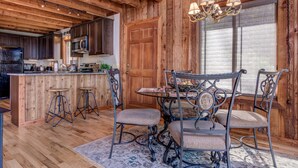 A rustic kitchen with wooden walls, a central island, bar stools, and a chandelier. - Suzie's Luxury Cabin Asheville HOT TUB  VIEWS  nr BILTMORE. (Asheville)