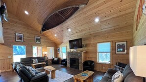 A cozy log cabin interior with a fireplace, leather sofas, a flat-screen TV, and wooden walls. - Home Theater, Hot tub & Huge Covered Patio! Stunning Home 2 Miles from Town! (Leavenworth)