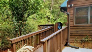Une terrasse en bois mène à un chalet doté d’une porte en métal et d’une fenêtre.
