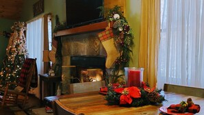 Un coin repas chaleureux avec une table en bois, des chaises, une cheminée et un sapin de Noël.