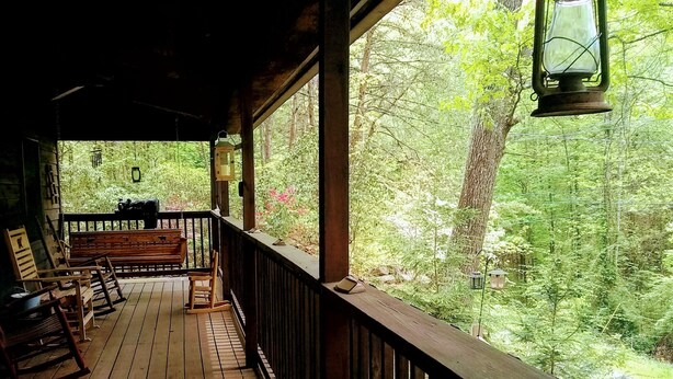 Une terrasse en bois, dotée de bancs et d’une lanterne, qui offre une vue sur une zone boisée.