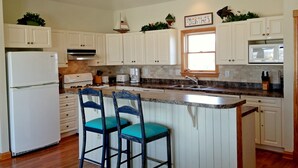 A kitchen with white cabinets, a refrigerator, a sink, and two blue chairs.