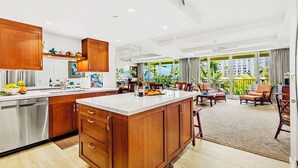 Une cuisine spacieuse dotée de meubles en bois et d’un grand îlot central, un coin repas offrant une vue sur les palmiers, et un salon avec une grande fenêtre donnant sur l’espace extérieur.