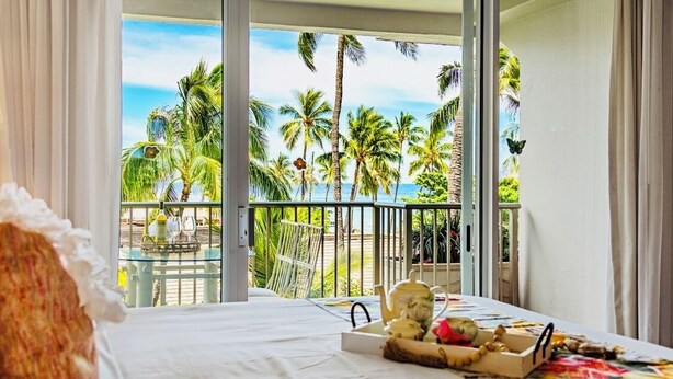Une chambre d’hôtel avec un balcon donnant sur des palmiers et l’océan.