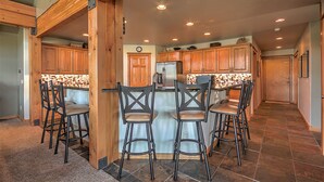 Une cuisine avec des meubles de rangement en bois, un îlot central doté de tabourets, et un mur recouvert de carreaux.