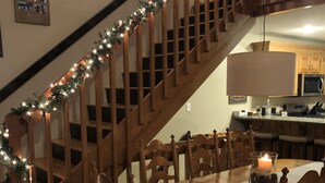 Una escalera de madera adornada con una guirnalda de luces, una mesa de comedor con sillas y un candelabro encendido en el centro.