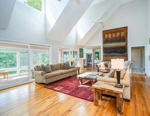 A spacious living room with a high ceiling, large windows, and a modern ceiling fan. - Huge Lodge, 1.5 Mi to town, Mtn Views, pets OK. (Asheville)